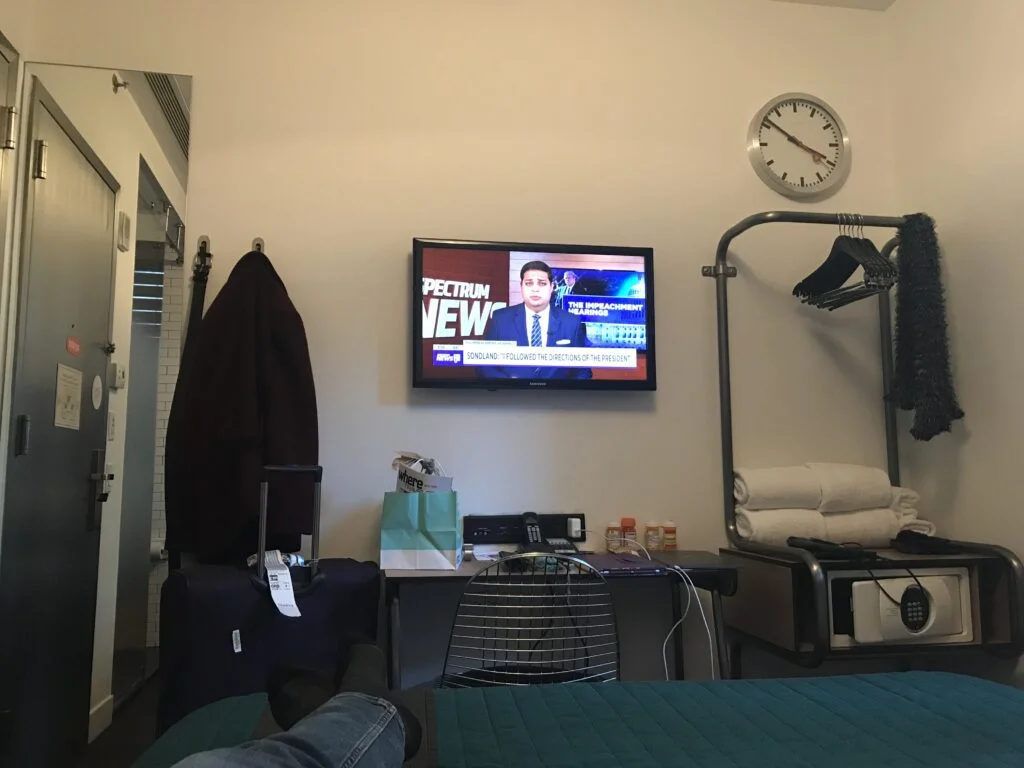 TV and Desk in Pod 39 Room: A small desk setup with a mounted TV in the Pod 39 hotel room, providing essentials in a limited space.