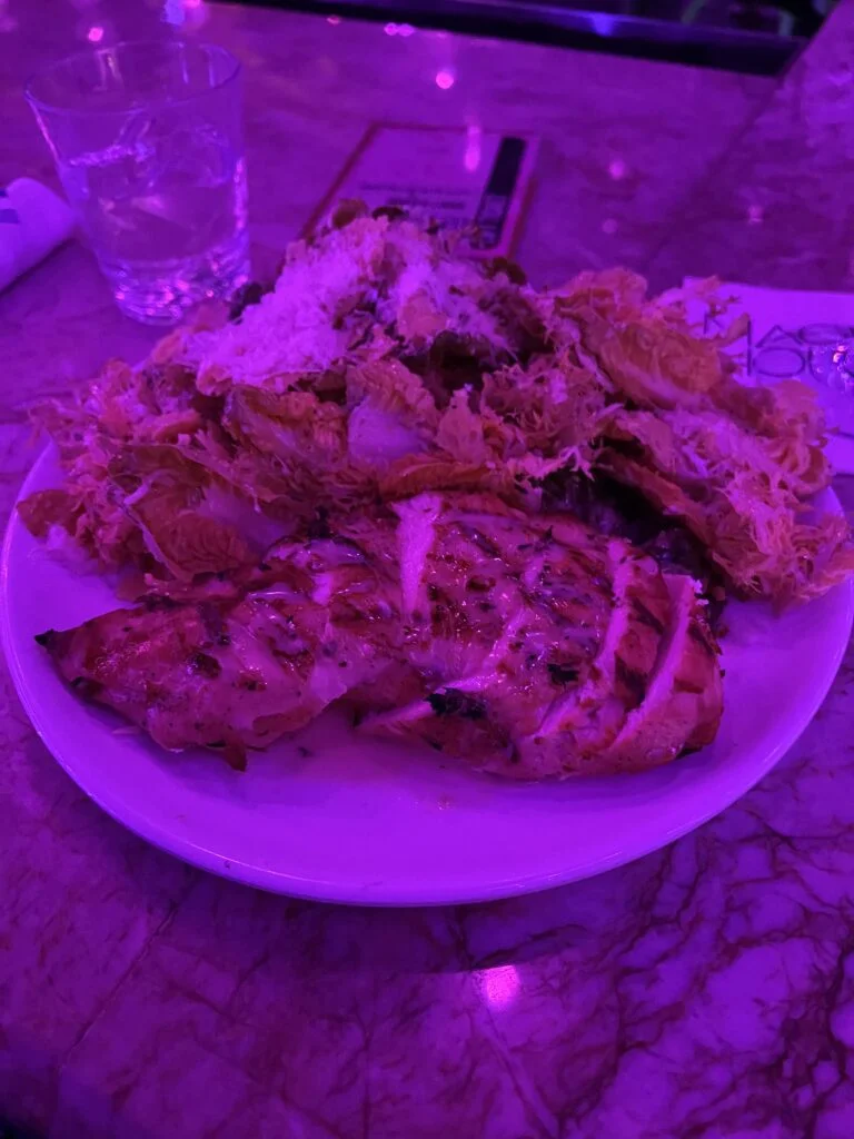 Chicken Caesar salad under pink lights at Magic Hour rooftop bar NYC