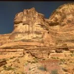 Towering red sandstone cliffs in Ruby Canyon, Colorado, viewed from the California Zephyr train under a deep blue sky.