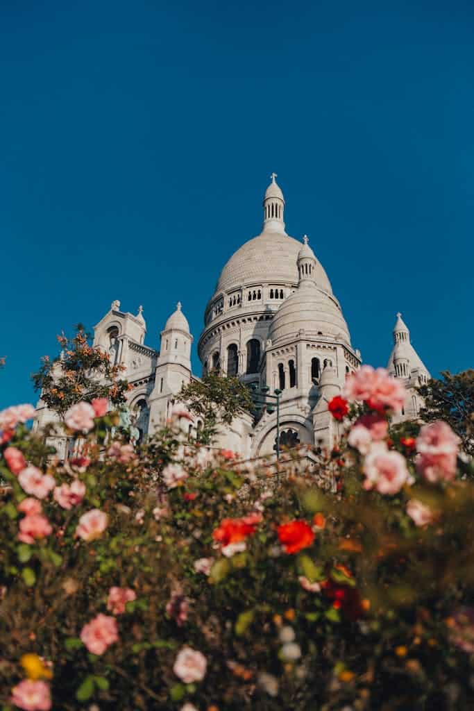 Planning a Trip to Paris 8 Stunning view of Sacré-Cœur Basilica framed by colorful flowers in Paris, under a clear blue sky.