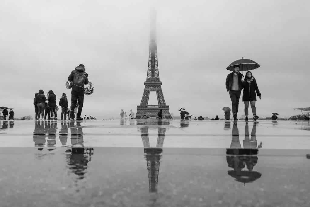Planning a Trip to Paris 3 Tourists with umbrellas near the Eiffel Tower on a rainy day in Paris.
