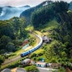 Aerial view of a picturesque train winding through lush green hills and rural houses.