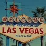 The famous Welcome to Las Vegas sign framed by palm trees under clear skies.