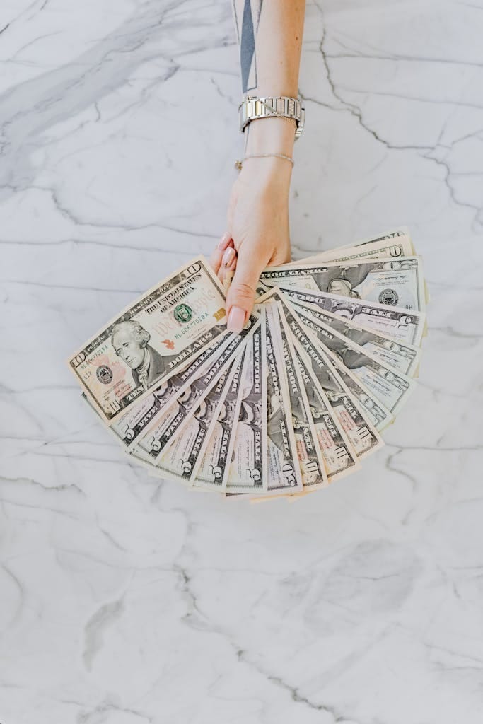 Travel Tips 3 A hand with wristwatch holding a fan of US dollar bills on a marble surface, symbolizing wealth and financial abundance.